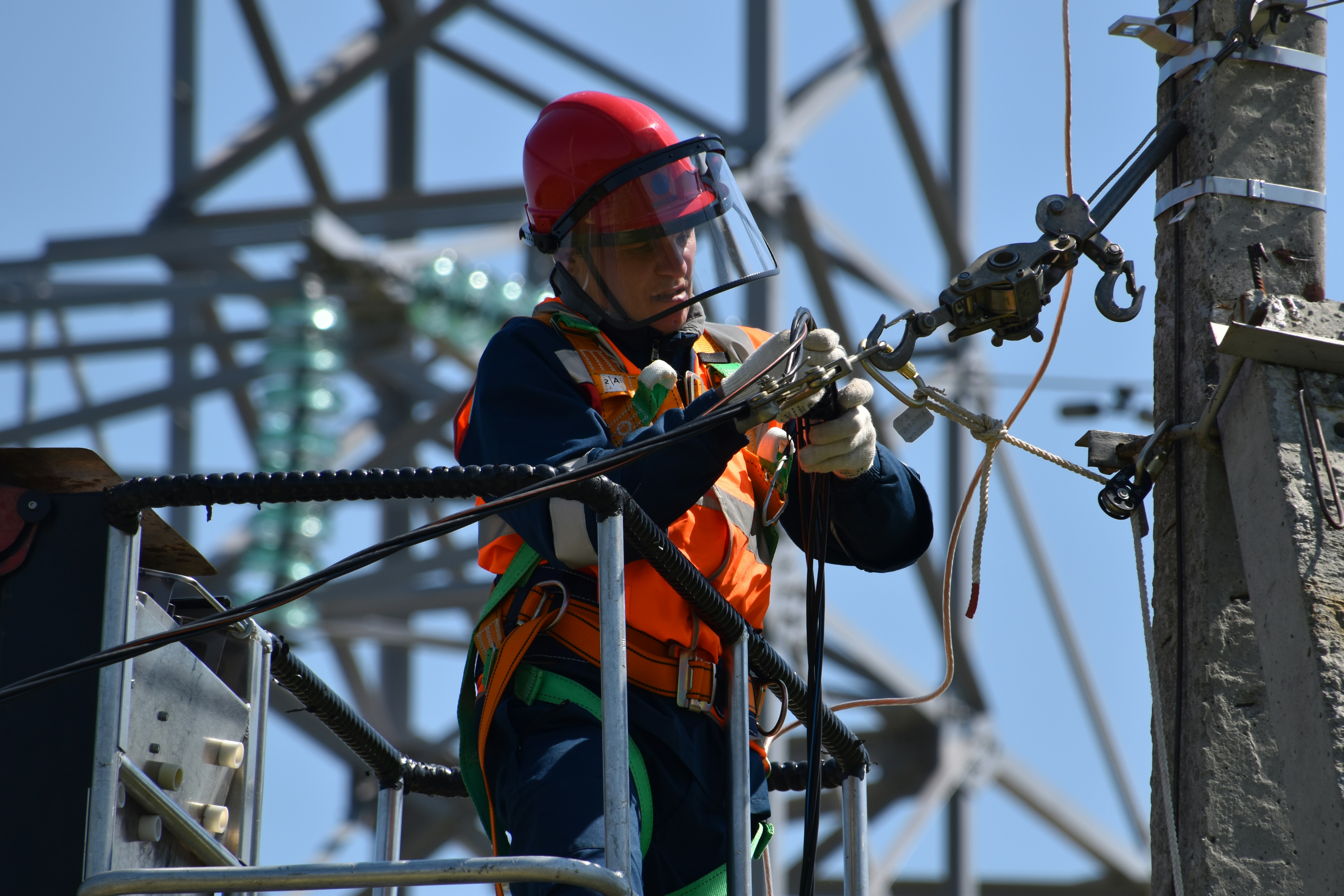 Elektryk w kasku i uprzęży na słupie energetycznym