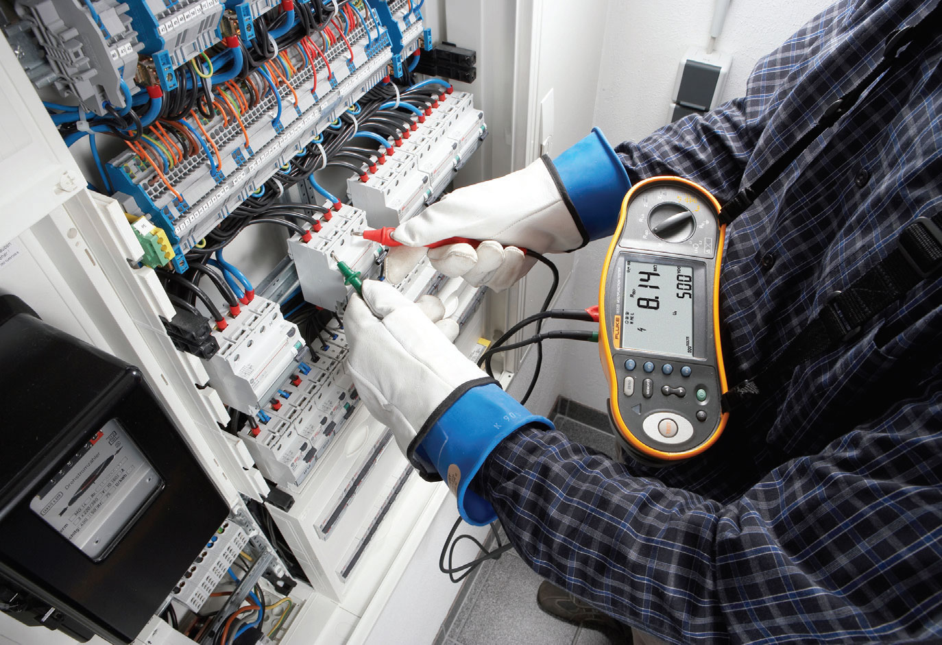 Elektryk wykonuje pomiary odbiorcze instalacji elektrycznej miernikiem przy rozdzielnicy